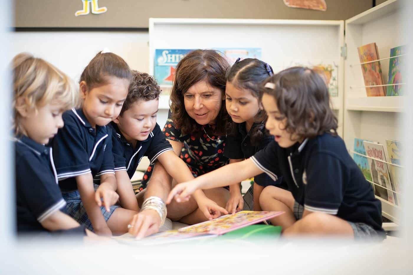 Young primary students and their teacher gathered around a table looking at books