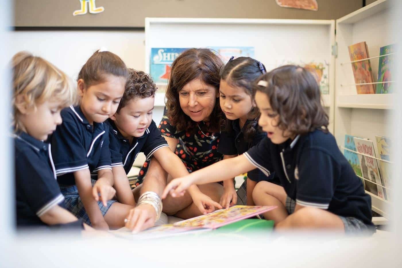 Young primary students and their teacher gathered around a table looking at books