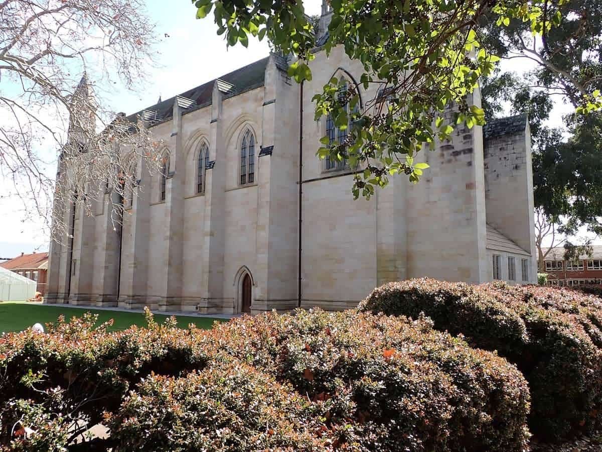 A heritage sandstone school chapel framed by trees and garden beds
