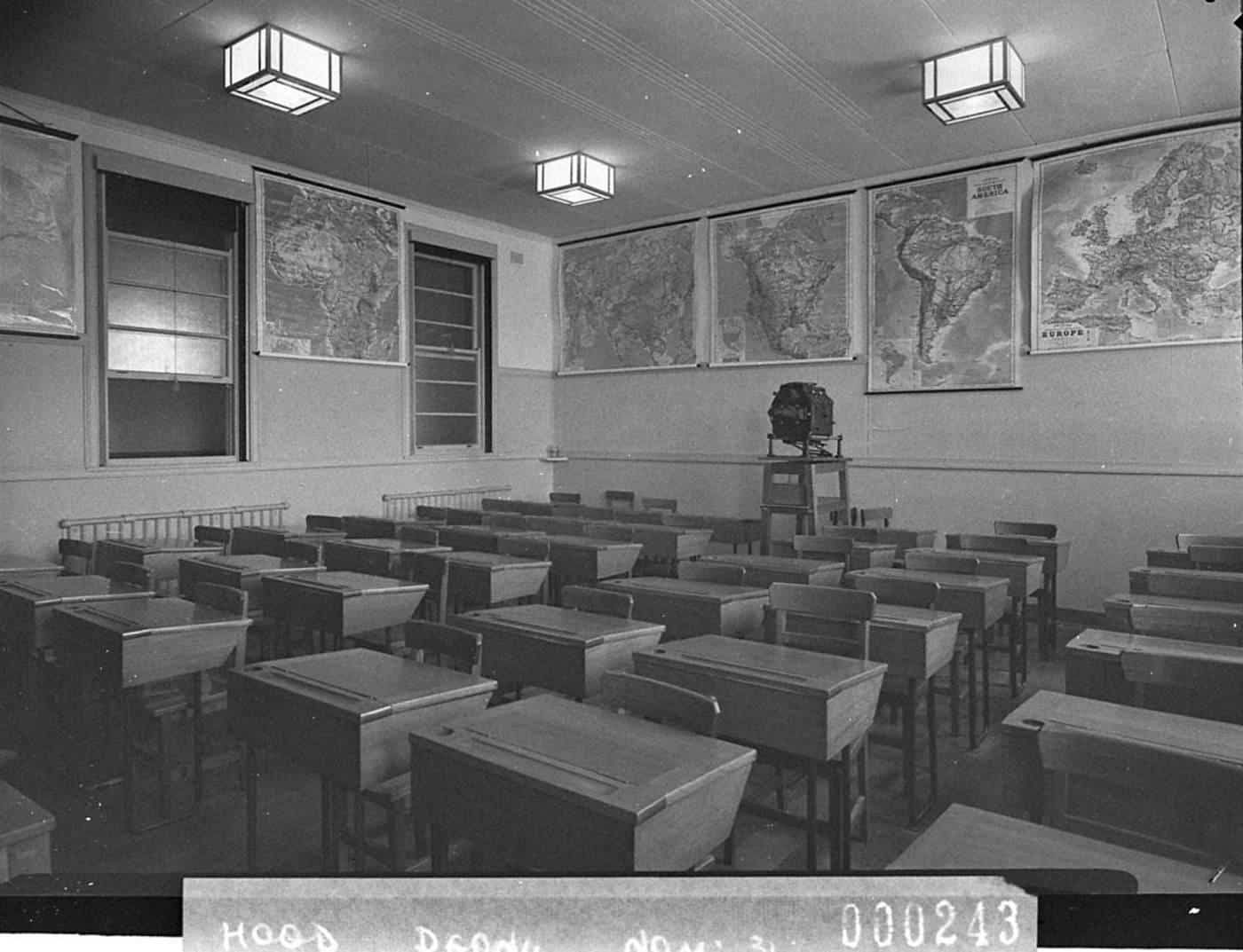 A historic Australian classroom with rows of timber desks and maps on the wall